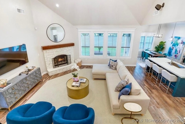 living area featuring high vaulted ceiling, visible vents, plenty of natural light, and wood finished floors