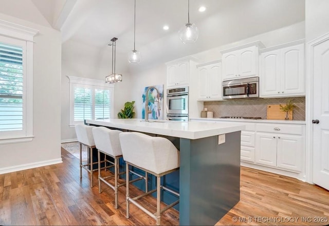 kitchen featuring white cabinets, appliances with stainless steel finishes, a kitchen island with sink, light countertops, and tasteful backsplash