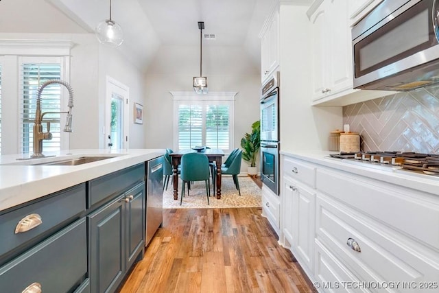 kitchen with appliances with stainless steel finishes, a sink, light wood finished floors, white cabinetry, and gray cabinetry