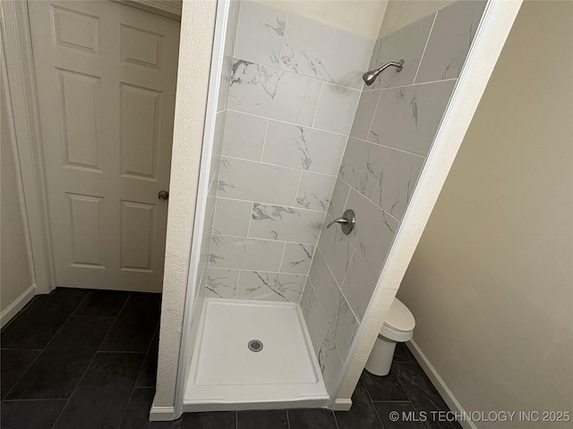 bathroom featuring tile patterned flooring, baseboards, a stall shower, and toilet