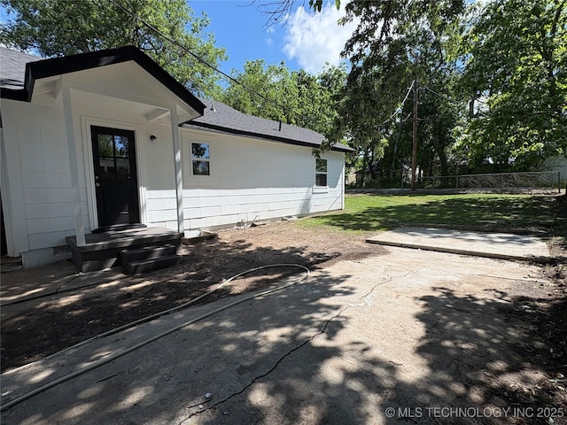 property entrance featuring a shingled roof, a patio area, fence, and a yard