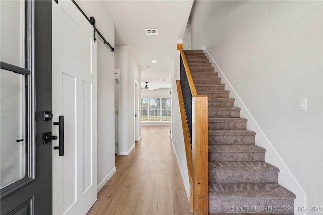 foyer with visible vents, baseboards, stairway, a barn door, and light wood-style flooring