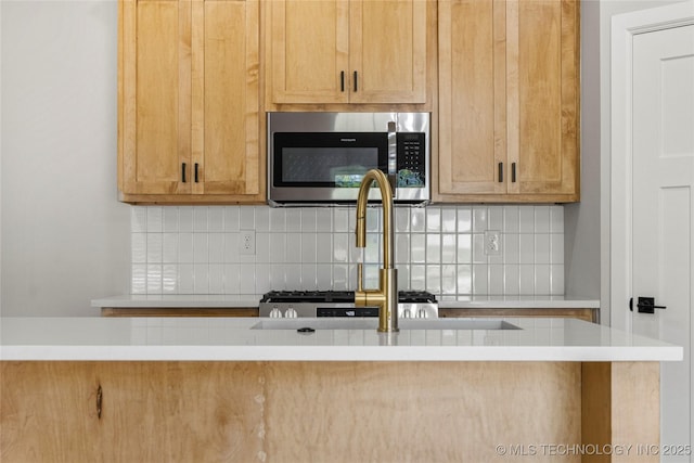 kitchen with backsplash, stainless steel microwave, a sink, and light countertops