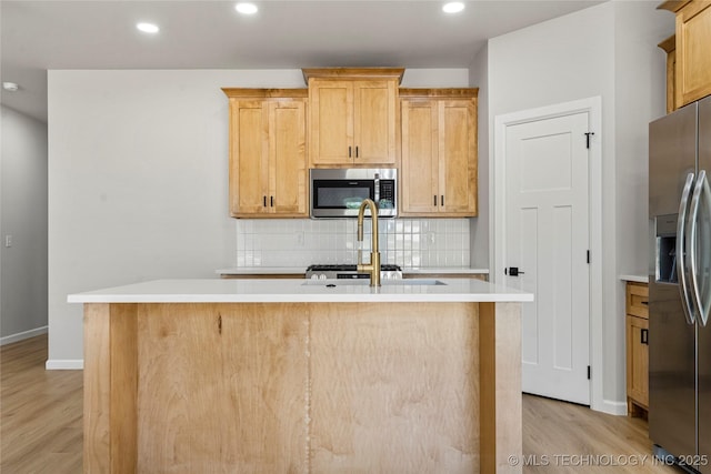 kitchen featuring decorative backsplash, a kitchen island with sink, light countertops, light wood-style floors, and stainless steel appliances