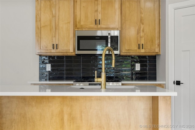 kitchen featuring backsplash, stainless steel microwave, a sink, and light countertops
