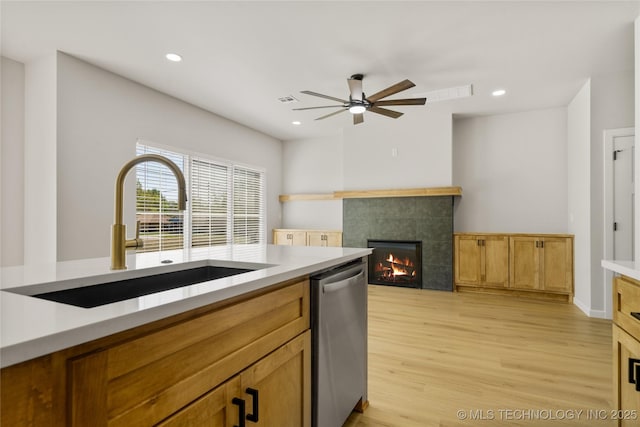 kitchen featuring a ceiling fan, a tiled fireplace, a sink, light wood-style flooring, and dishwasher