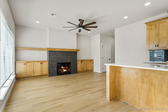 interior space with light wood finished floors, a ceiling fan, recessed lighting, a tile fireplace, and visible vents