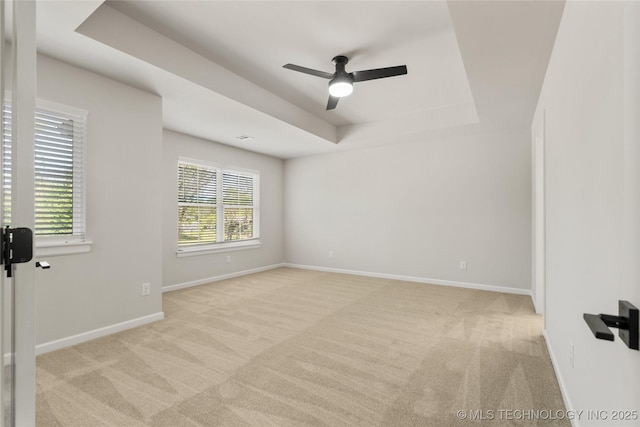 unfurnished room featuring a raised ceiling, baseboards, light carpet, and a ceiling fan