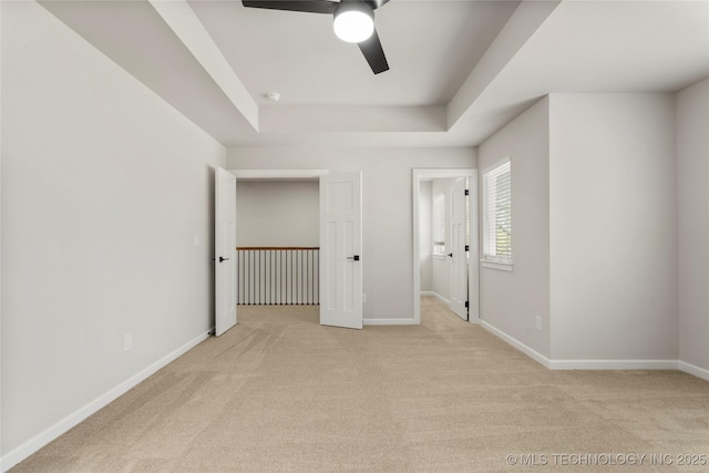 unfurnished bedroom with carpet flooring, a tray ceiling, and baseboards