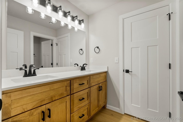 full bathroom featuring double vanity, a sink, baseboards, and wood finished floors
