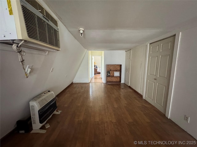 unfurnished living room with heating unit, a wall mounted air conditioner, and wood finished floors