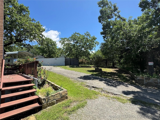 view of yard with a deck, driveway, fence, and a carport