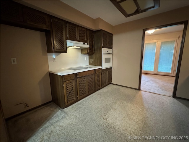 kitchen with dark brown cabinetry, light countertops, baseboards, under cabinet range hood, and oven