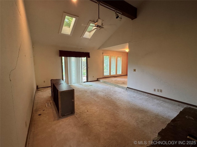 carpeted spare room featuring a skylight, beam ceiling, track lighting, baseboards, and high vaulted ceiling