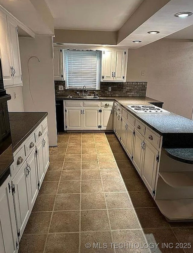 kitchen featuring open shelves, a sink, white electric cooktop, a peninsula, and decorative backsplash