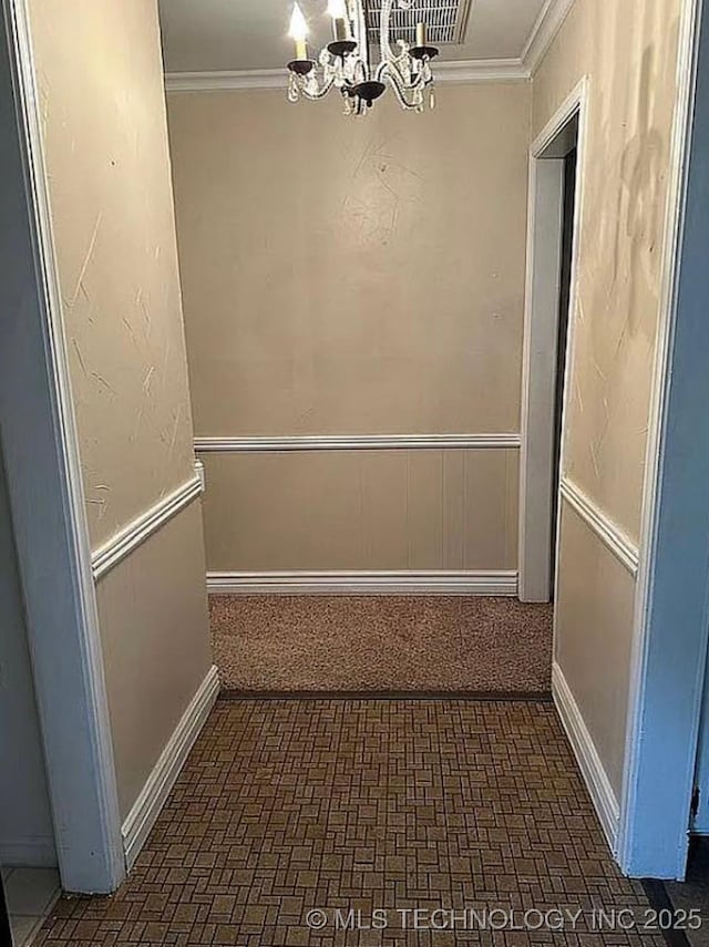hallway featuring crown molding, an inviting chandelier, and brick patterned floor