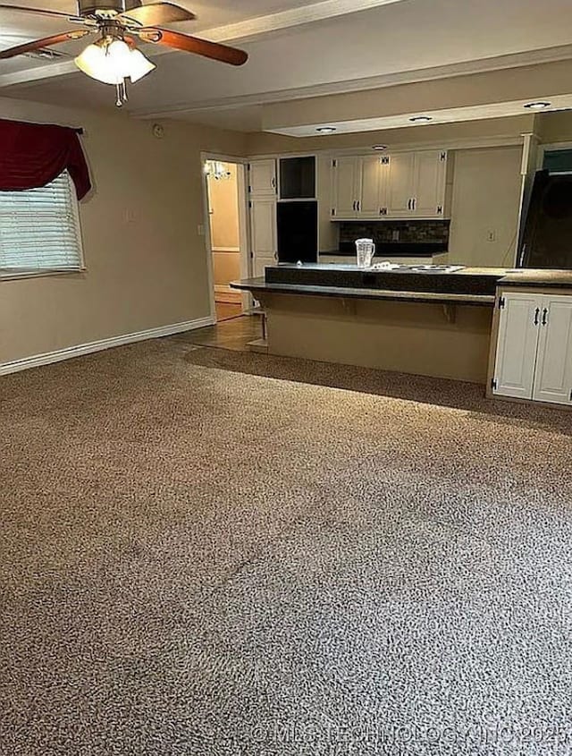 kitchen with white cabinets, ceiling fan, a breakfast bar, dark countertops, and baseboards