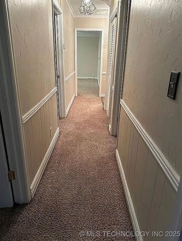 hallway featuring light colored carpet, ornamental molding, a decorative wall, and a wainscoted wall