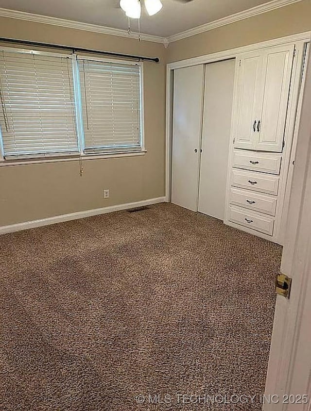 unfurnished bedroom featuring crown molding, ceiling fan, carpet, baseboards, and a closet