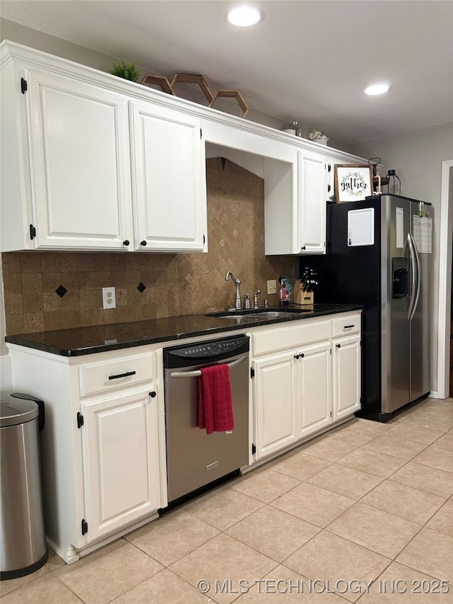 kitchen with appliances with stainless steel finishes, tasteful backsplash, dark countertops, a sink, and white cabinets