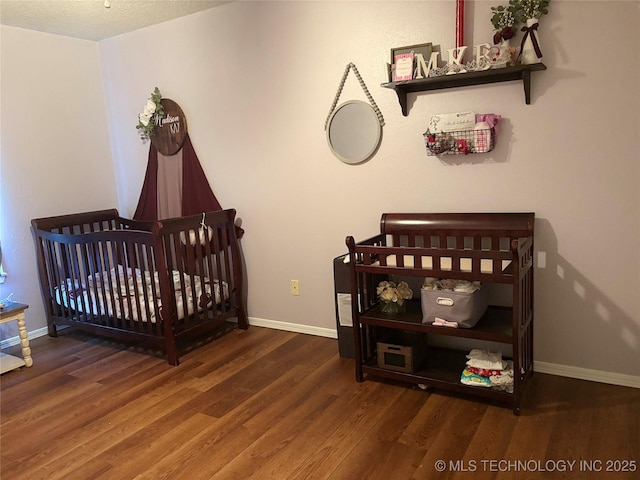 bedroom featuring baseboards, wood finished floors, and a crib