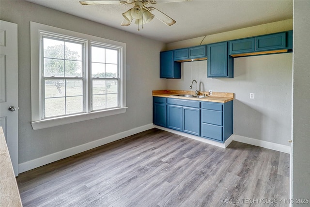 kitchen featuring a ceiling fan, baseboards, a sink, light wood finished floors, and blue cabinetry