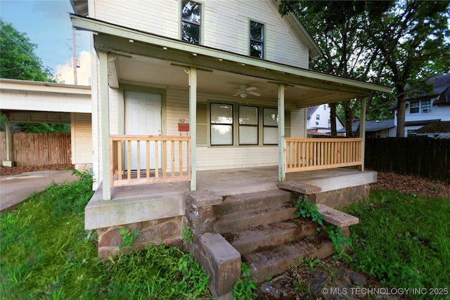 doorway to property featuring fence, a ceiling fan, covered porch, and a carport
