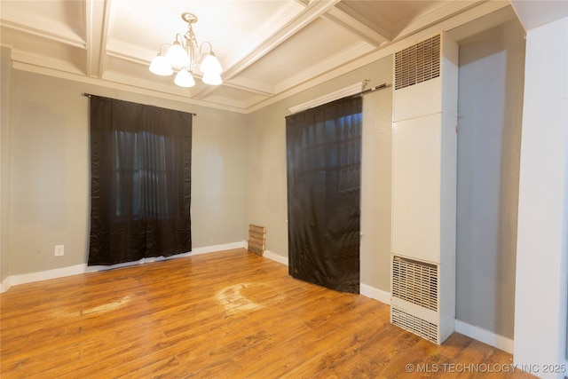 spare room featuring an inviting chandelier, a heating unit, coffered ceiling, and wood finished floors