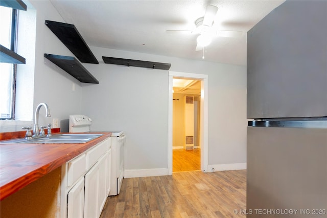 kitchen featuring freestanding refrigerator, open shelves, butcher block countertops, white electric range oven, and a sink