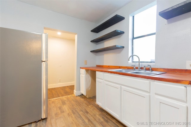 kitchen with wooden counters, a sink, white cabinets, freestanding refrigerator, and light wood-style flooring