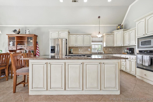 kitchen featuring ornamental molding, dark stone countertops, appliances with stainless steel finishes, and cream cabinetry