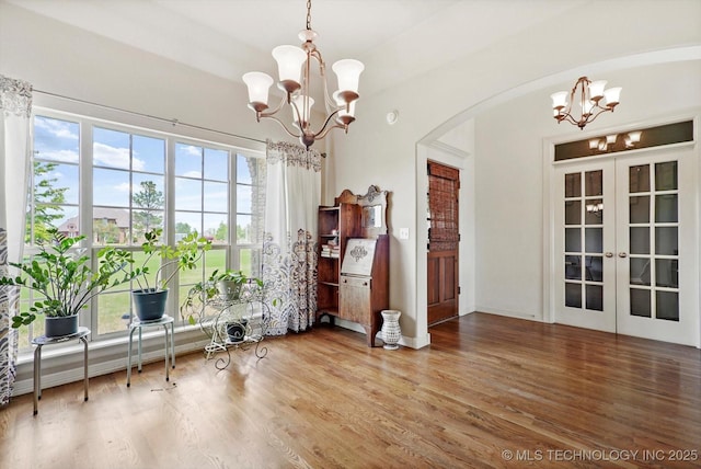 dining room featuring french doors, arched walkways, wood finished floors, and a notable chandelier