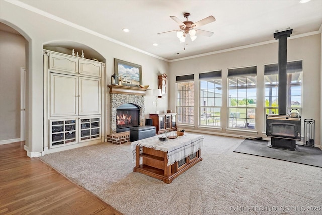 living room featuring baseboards, ornamental molding, a ceiling fan, and a wood stove