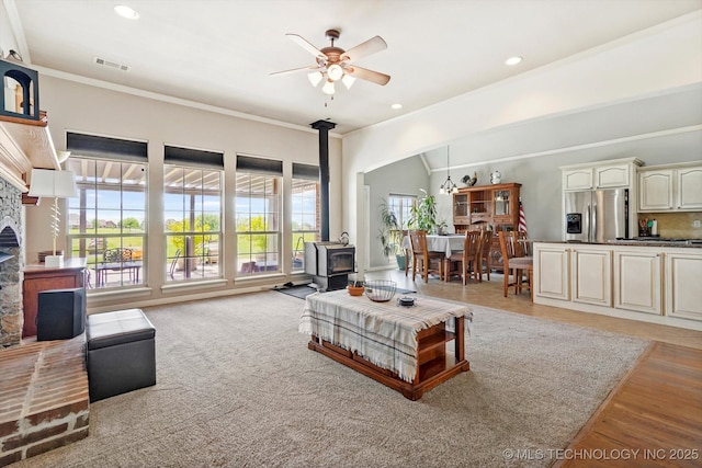 living room featuring ceiling fan, a wood stove, recessed lighting, visible vents, and ornamental molding