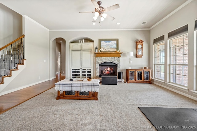 carpeted living area with a ceiling fan, crown molding, arched walkways, a fireplace, and baseboards