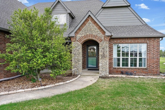 view of front facade featuring roof with shingles, stone siding, a front yard, and brick siding
