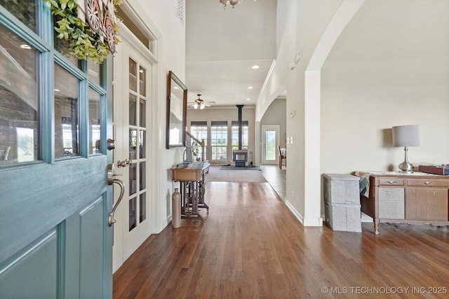 foyer entrance featuring arched walkways, ceiling fan, wood finished floors, and a wood stove