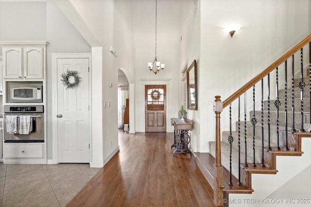 entryway featuring arched walkways, wood finished floors, an inviting chandelier, a high ceiling, and stairs