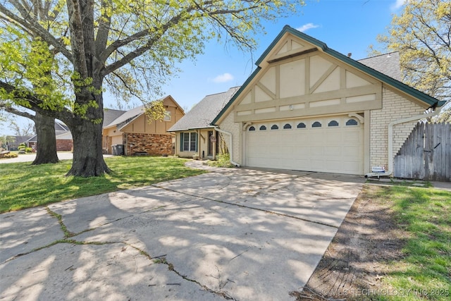 tudor house with fence, brick siding, a garage, a front yard, and driveway