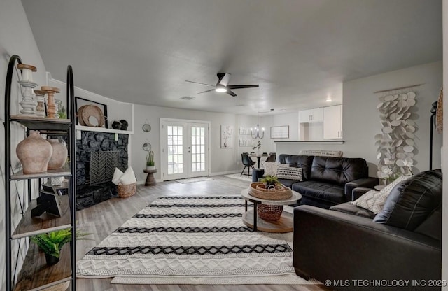 living room featuring visible vents, a fireplace, baseboards, ceiling fan with notable chandelier, and light wood-style flooring