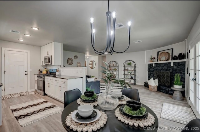 dining space with baseboards, light wood-type flooring, a stone fireplace, and visible vents