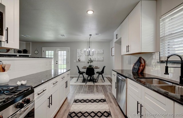 kitchen with white cabinetry, a sink, light wood finished floors, a notable chandelier, and stainless steel appliances