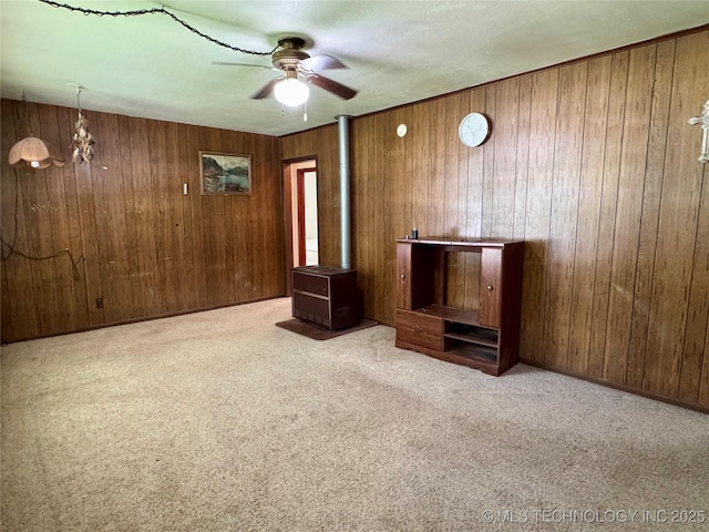 unfurnished living room featuring a ceiling fan, carpet flooring, wood walls, and a chandelier