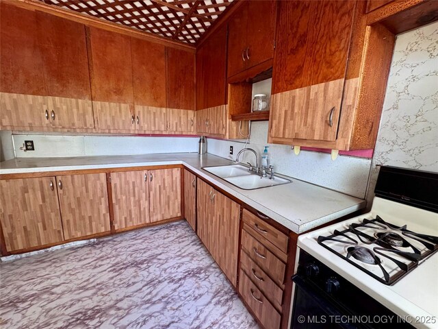 kitchen featuring range with gas cooktop, a sink, light countertops, open shelves, and wallpapered walls