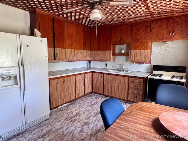kitchen with white fridge with ice dispenser, gas stove, a sink, a ceiling fan, and light countertops
