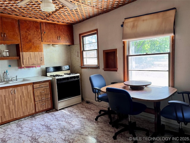 kitchen with white range with gas stovetop, a sink, light countertops, and healthy amount of natural light