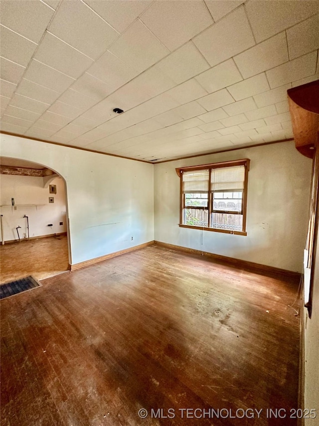unfurnished room featuring arched walkways, baseboards, and wood finished floors
