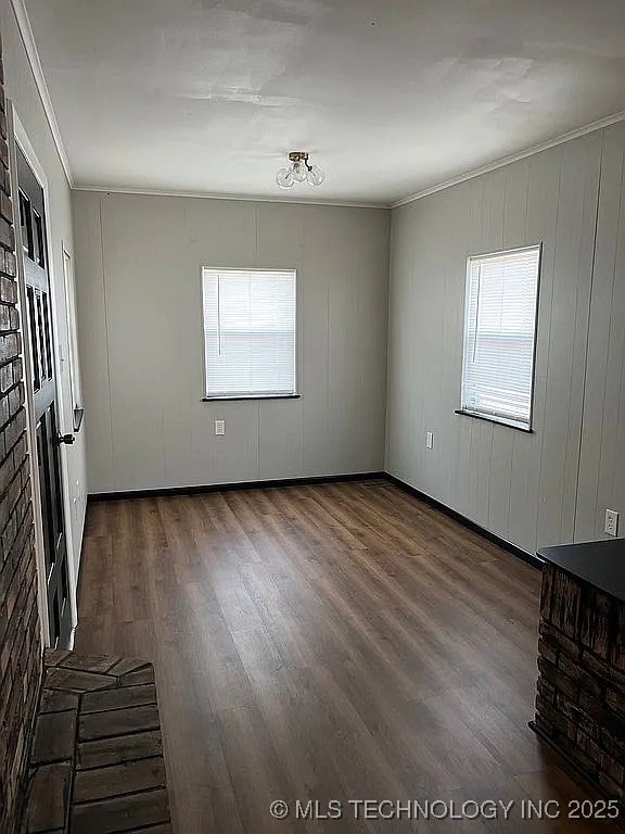 empty room featuring plenty of natural light, ornamental molding, and dark wood-type flooring