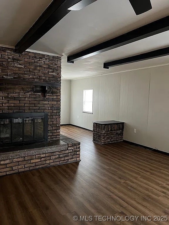 unfurnished living room with baseboards, a fireplace, beam ceiling, and wood finished floors