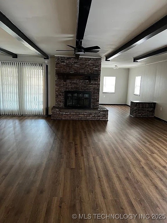 unfurnished living room with a ceiling fan, beamed ceiling, a brick fireplace, and wood finished floors